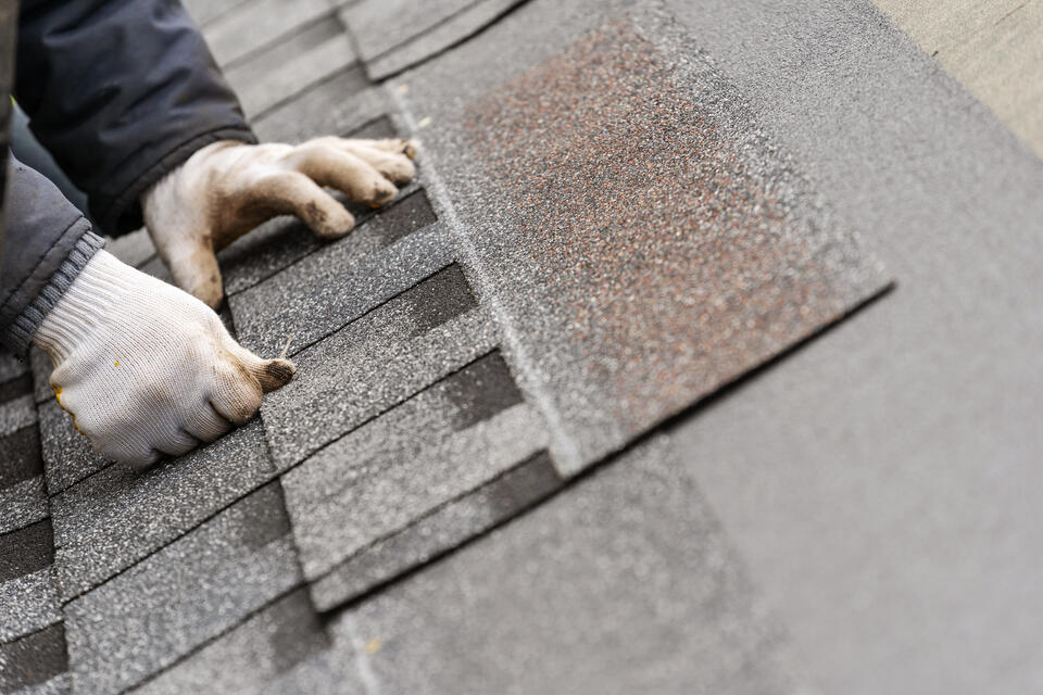 roof replacement cost-close up of a gloved hand installing new shingles
