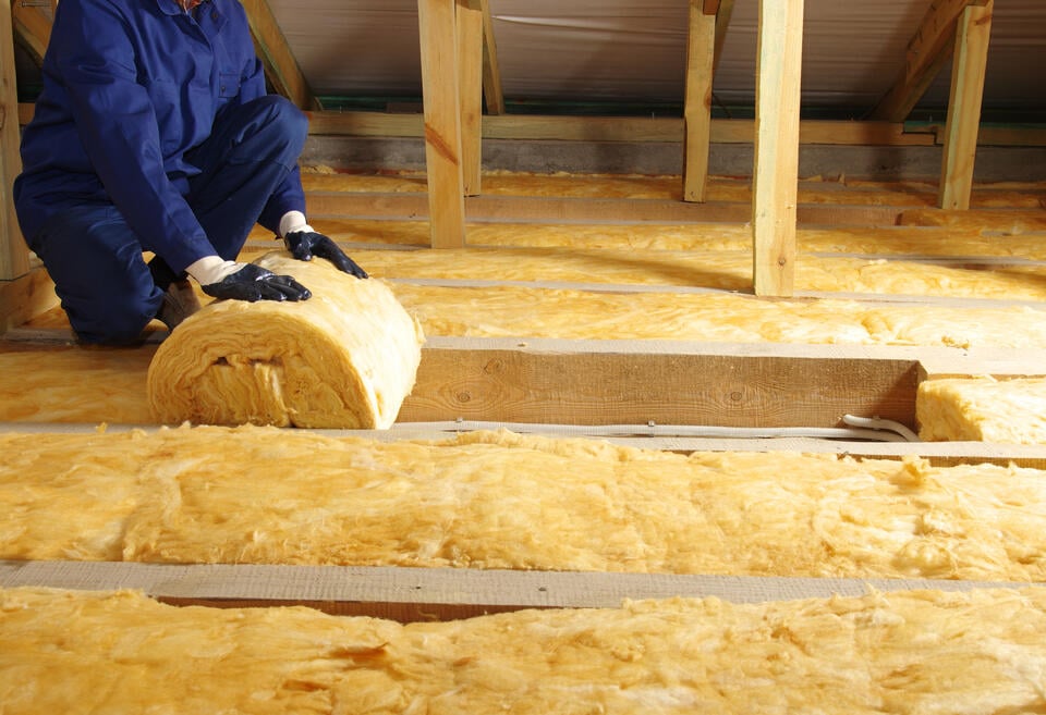 attic insulation cost-technician unrolling a section of insulation into attic floor