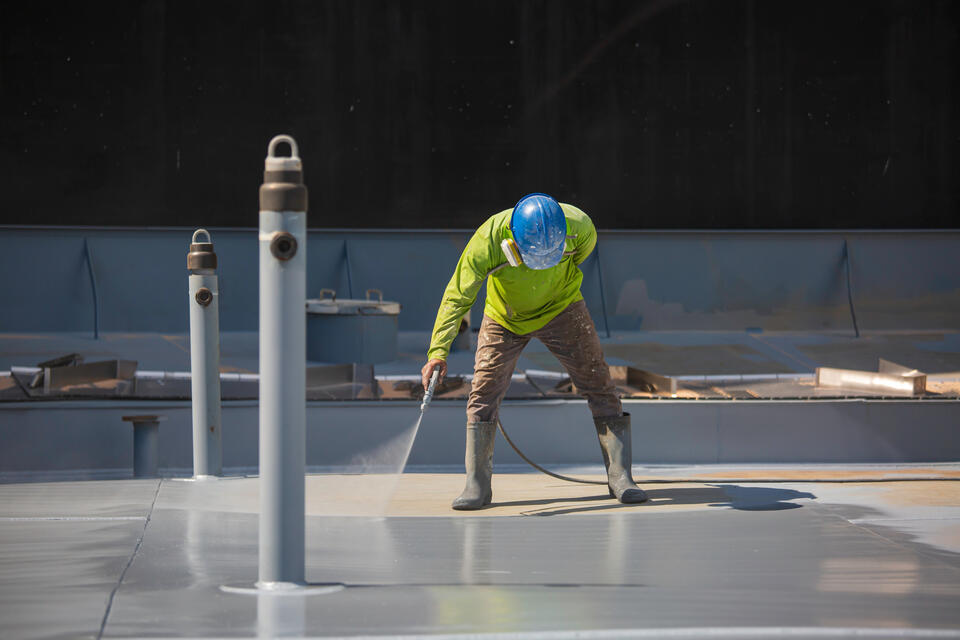 roof coating-man wearing hard hat spraying flat roof with coating