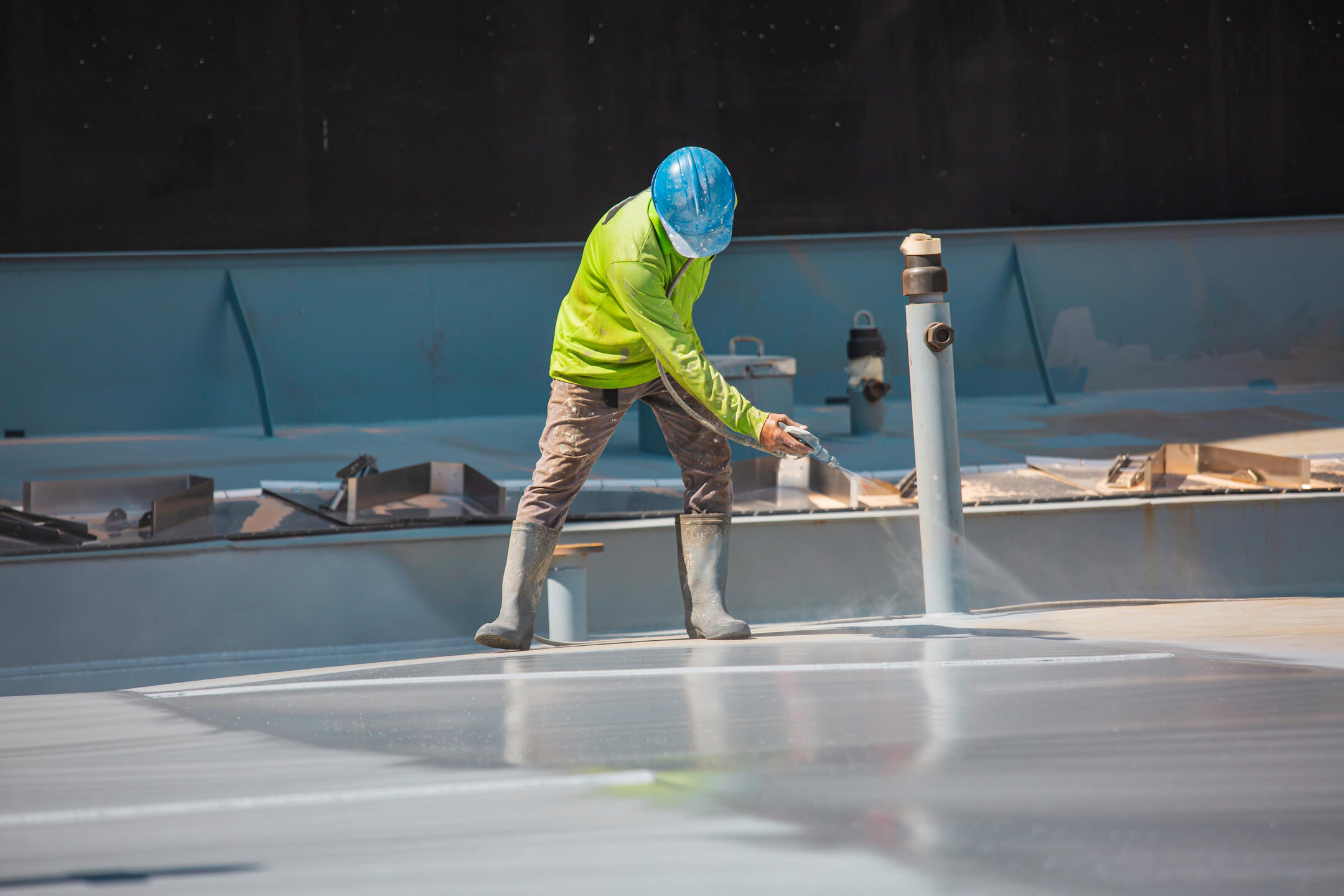 roof coating-man wearing protective gear spraying flat roof with coating