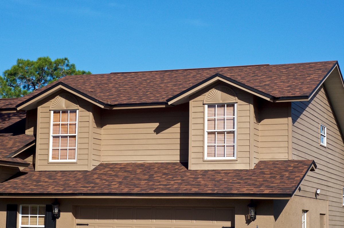 View of generic brown two story American house against blue sky with gables windows.