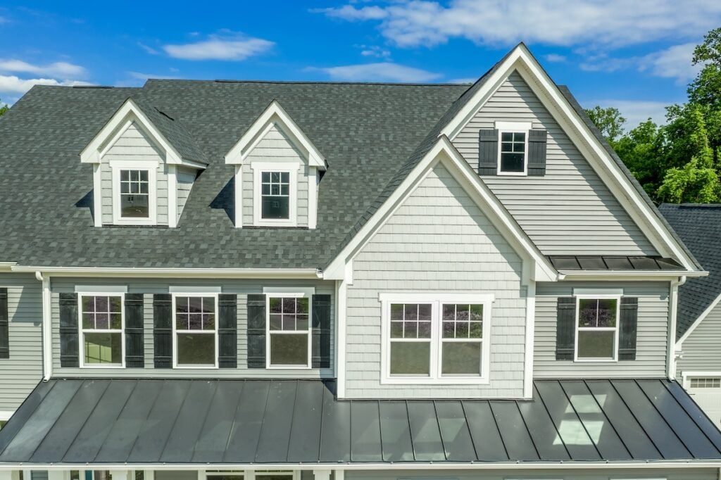 Classic American real estate single family home facade  with horizontal vinyl siding, dormer windows, double gable, double and single sash windows, blue cloudy background
