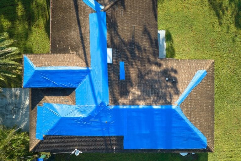 Top view of leaking house roof covered with protective tarp sheets against rain water leaks until replacement of asphalt shingles. Damage of building rooftop as aftermath of hurricane Ian in Florida.