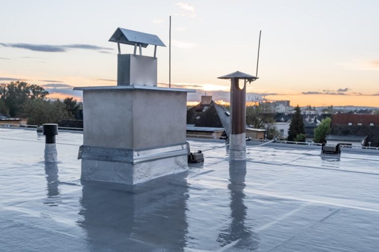 Flat roof covered with bitumen membrane and silver lacquer with chimney on a private house. Reflections on roof after rain