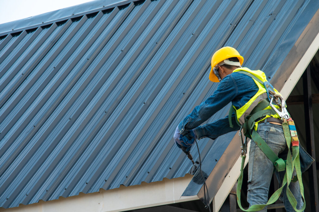 Construction worker wearing safety harness belt during working on roof structure of building on construction site,Roofer using air or pneumatic nail gun and installing metal roof tile on top new roof. commercial roof replacement 