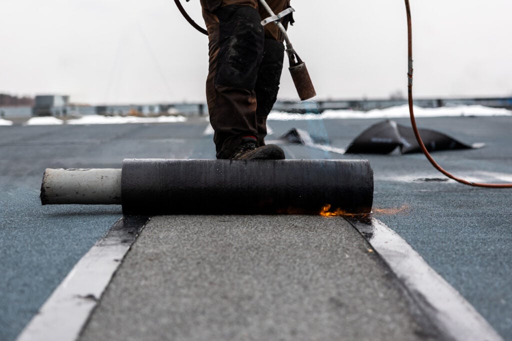 professional roofer at work securing rolled tar paper with a blowtorch on a flat roof installation process rubber roofing