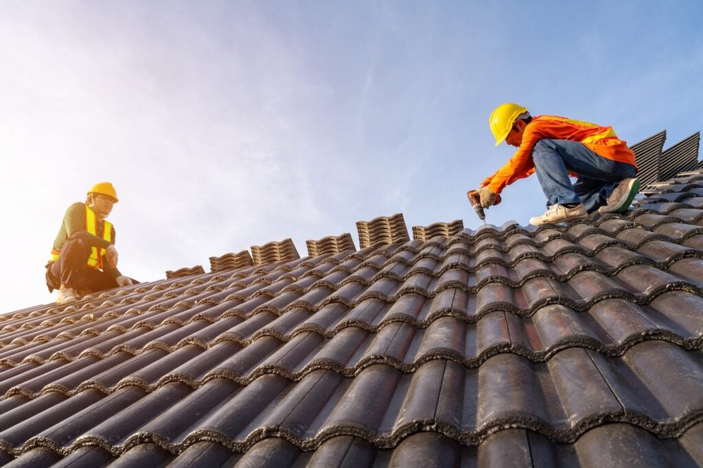 Two Roofer working on roof structure of building on construction site,Roofer using air or pneumatic nail gun and installing Concrete Roof Tiles on top new roof. roofing contractors panama city fl