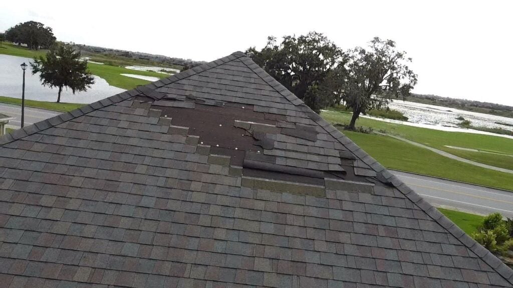 Residential roof with large sections of missing asphalt shingles after severe weather