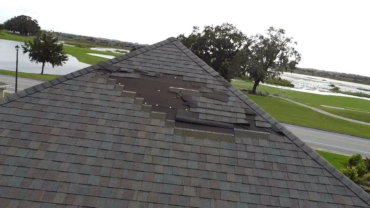 Storm-damaged asphalt shingle roof with missing shingles and exposed underlayment