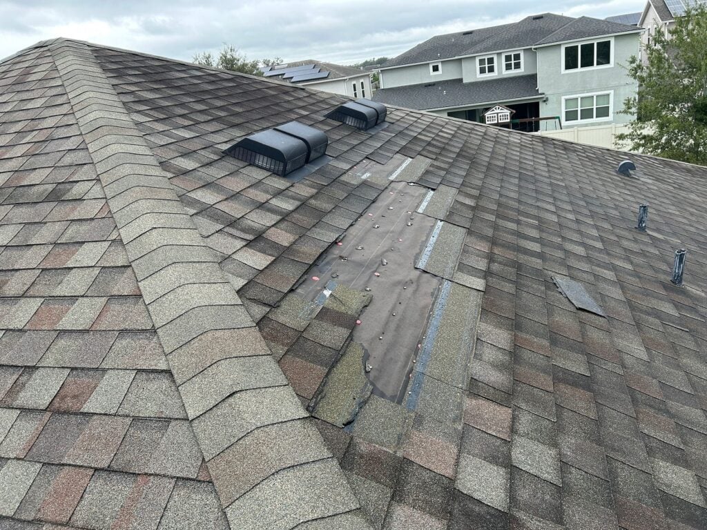 Storm-damaged asphalt shingle roof with exposed underlayment and missing shingles