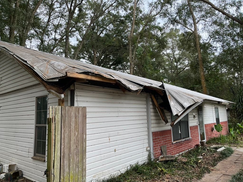 Home with severe structural roof damage, collapsed decking, and exposed framing
