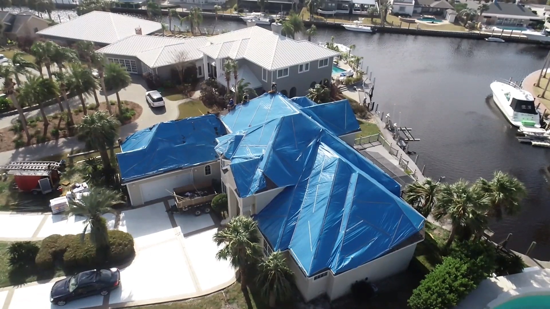 Aerial view of blue emergency roof tarps protecting a storm-damaged waterfront home in Tampa, Florida