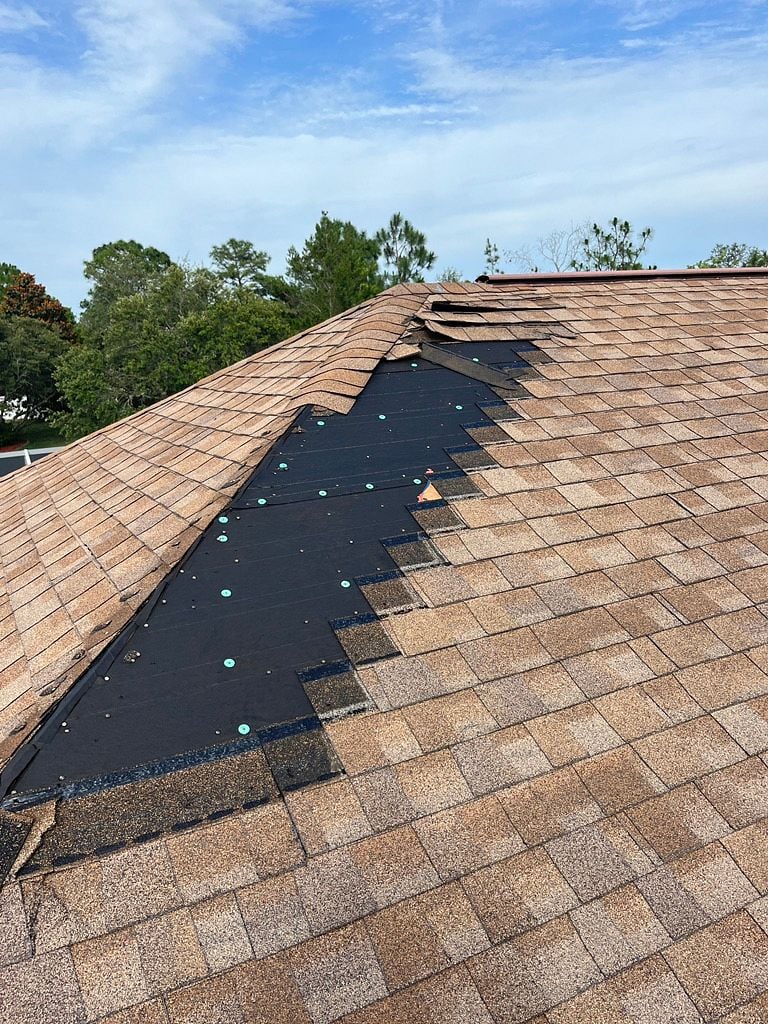 Asphalt shingle roof with missing shingles and exposed underlayment after storm damage