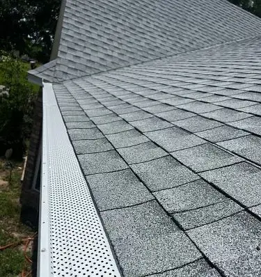 White gutter and perforated gutter guard installed along a gray asphalt shingle roof