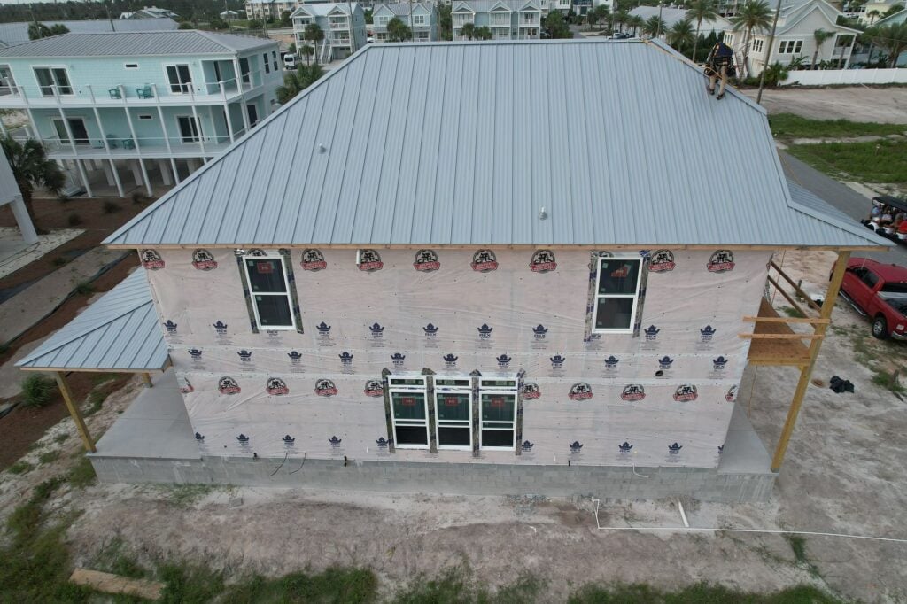Side view of a two-story home with fresh weather wrapping and a blue-gray standing seam metal roof in Mexico Beach, FL.
