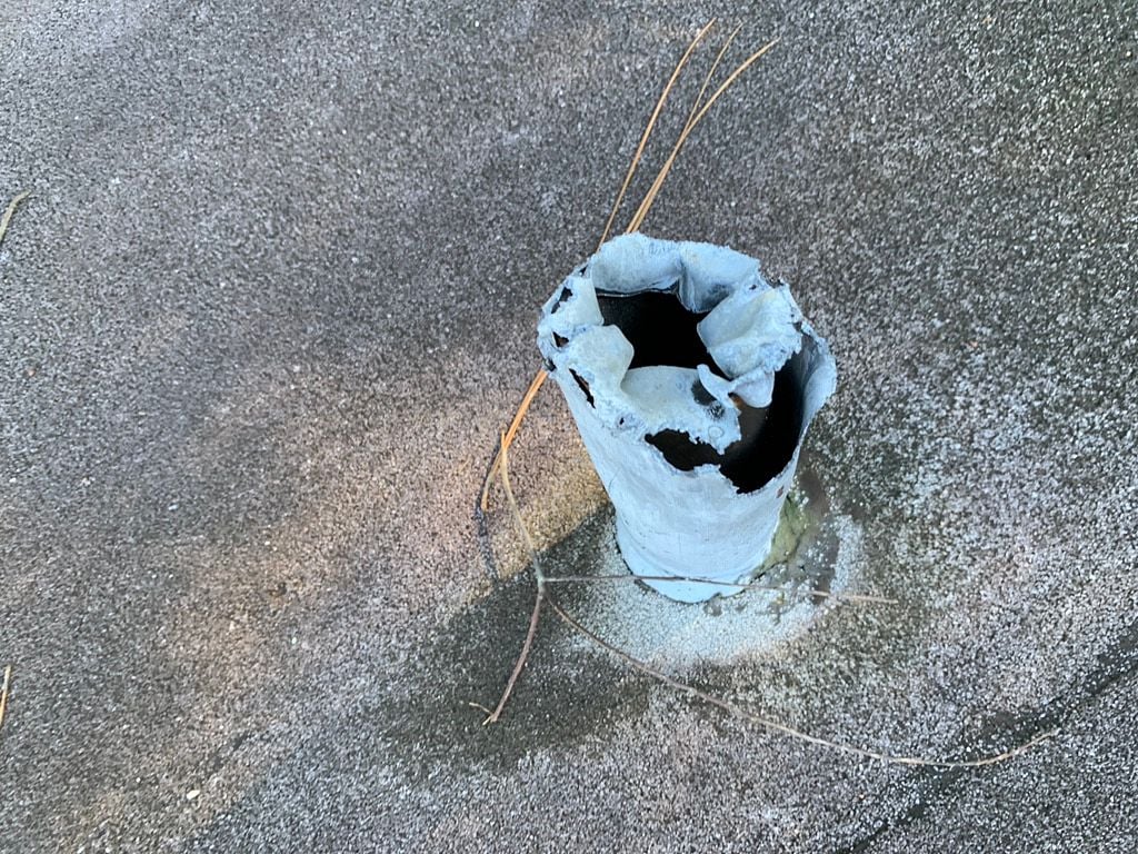 Damaged pipe boot with torn flashing on a flat roof before repair
