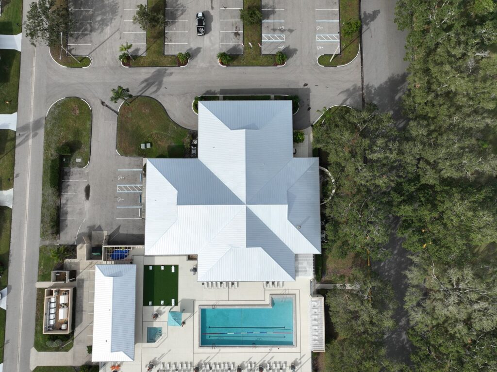 Top-down aerial view of a 24-gauge standing seam metal roof installation on a cross-shaped commercial clubhouse in Sarasota, FL.