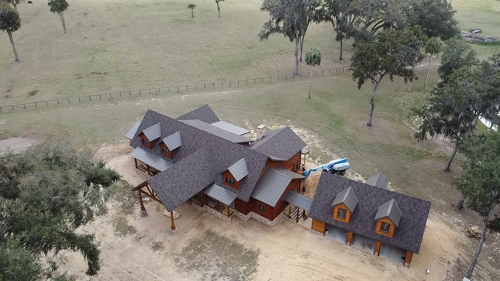High aerial drone shot of a log home estate in Reddick, FL featuring CertainTeed Presidential IR shingles and metal roof accents.